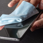 Person using microfiber cloth to wipe phone screen.
